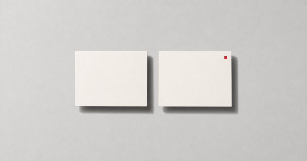 Two identical off-white cards lying flat, one plain and one carrying a small red mark in its corner.